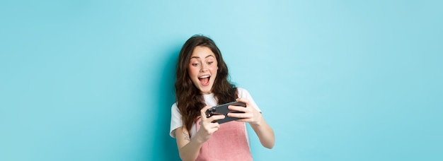 Free Photo portrait of excited young woman playing mobile video game with both hands smiling amused looking at