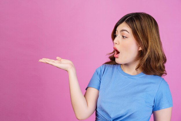 Portrait of excited young woman wearing casual tshirt hold hand demonstrate offer ads promo isolated over pink background