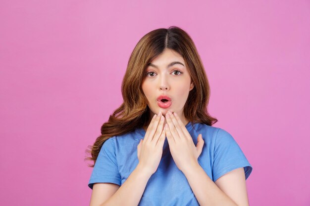 Portrait of excited young woman wearing casual tshirt surprising isolated over pink background