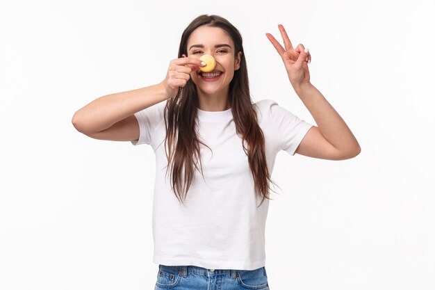 portrait expressive young woman holding tasty two macarons over eyes