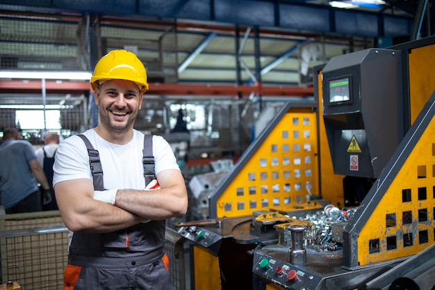 Portrait of factory worker with arms crossed standing by industrial machine in production plant