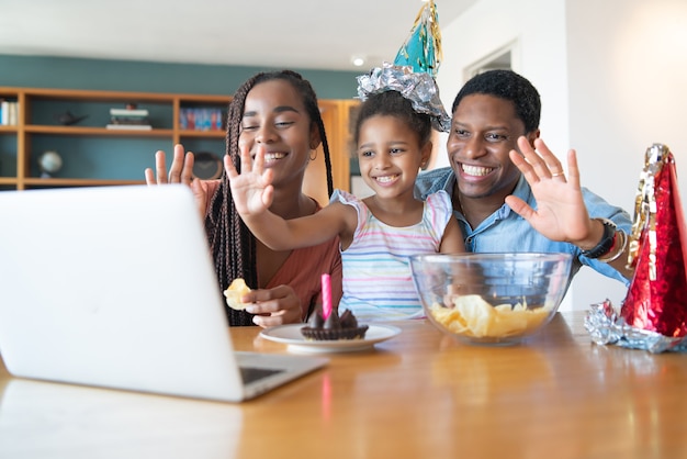 Portrait of a family celebrating birthday online on a video call with laptop while staying at home. New normal lifestyle concept.