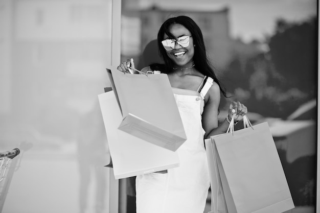 Free Photo portrait of a fantastic african american woman wearing sunglasses holds multicolored shopping bags outside the mall black and white photo