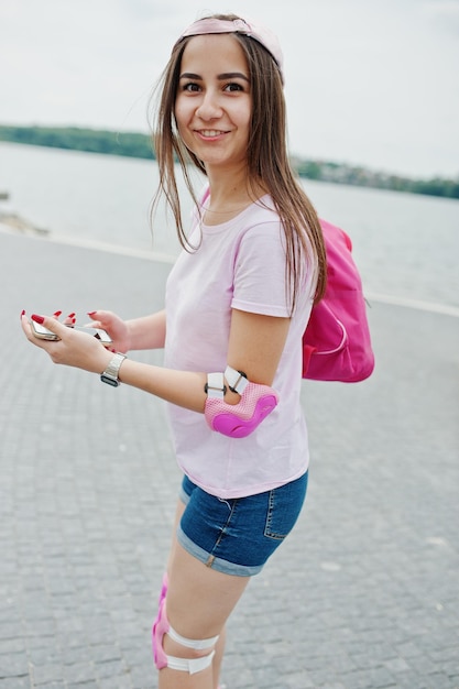 Portrait of a fantastic young woman roller skating with her phone in her hands in the park next to the lake