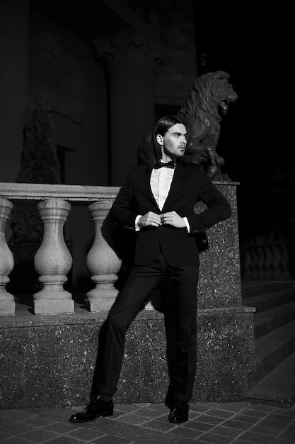 Free photo portrait of fashion elegant long-haired young man. attractive and handsome male model in black suit with mustache in the street at night