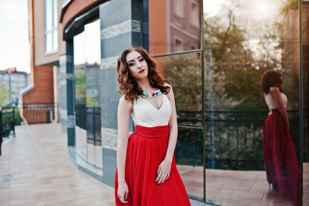 Free photo portrait of fashionable girl at red evening dress posed background mirror window of modern building