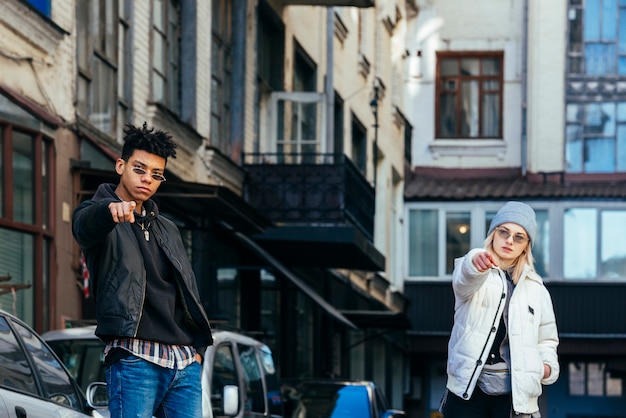 Portrait of fashionable teenage couple pointing their fingers toward camera