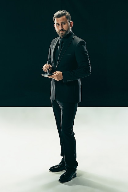 Portrait of a fashionable young man with stylish haircut wearing trendy suit posing over black.