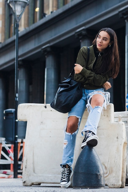 Free photo portrait of a fashionable young woman with bag sitting on street