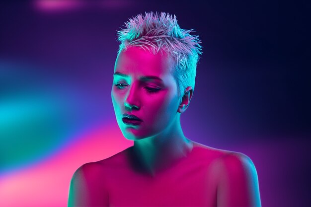 Portrait of female fashion model in neon light on dark studio background.