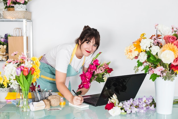 Portrait of a female florist with flowers writing on notepad