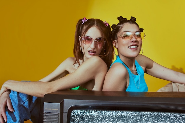 Free photo portrait of female friends in 2000s fashion style posing together with tv