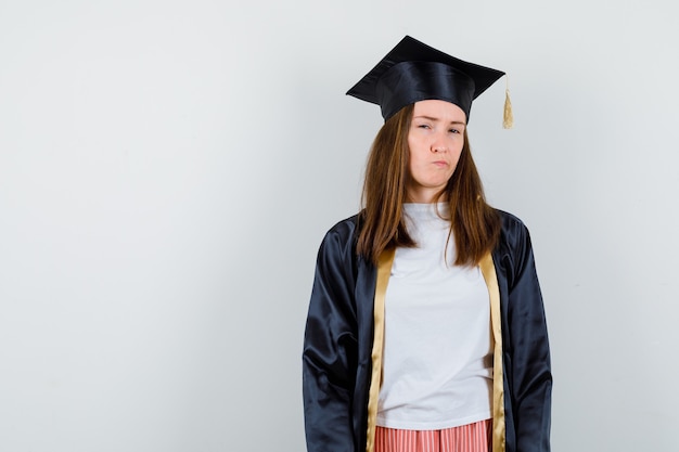 Free photo portrait of female graduate looking at camera, curving lips in academic dress and looking pensive front view