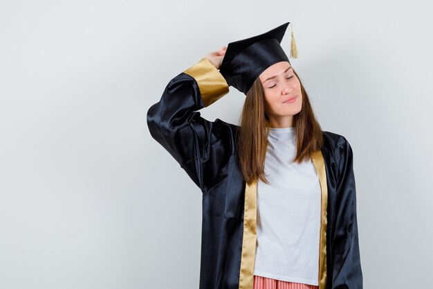 Portrait of female graduate posing with raised hand on head in uniform, casual clothes and looking charming front view