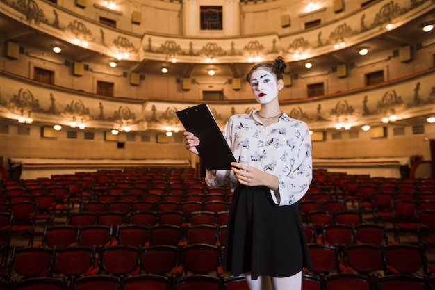 Portrait of female mime standing in an auditorium holding script