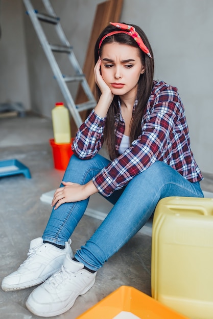 Free photo portrait of female painter sitting on floor near wall after painting