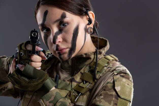 Portrait of female soldier in military uniform with gun on dark wall