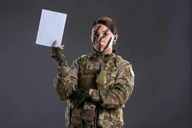 Portrait of female soldier with letter in her hands on dark wall