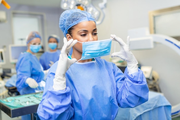 Free Photo portrait of female surgeon wearing surgical mask and cap skilled doctor is working in illuminated operating room she is in hospital