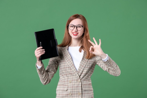 Portrait of female teacher holding notepad on green