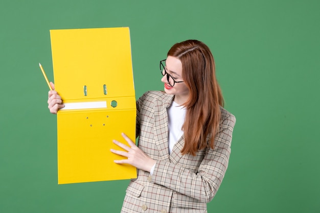 Free Photo portrait of female teacher holding open yellow document on green