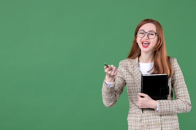 Portrait of female teacher with notepad in great mood on green