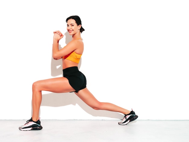 Portrait of fitness smiling woman in black sports clothing Sexy young beautiful model with perfect body Female isolated on white wall in studio Stretching out before training Doing lunges