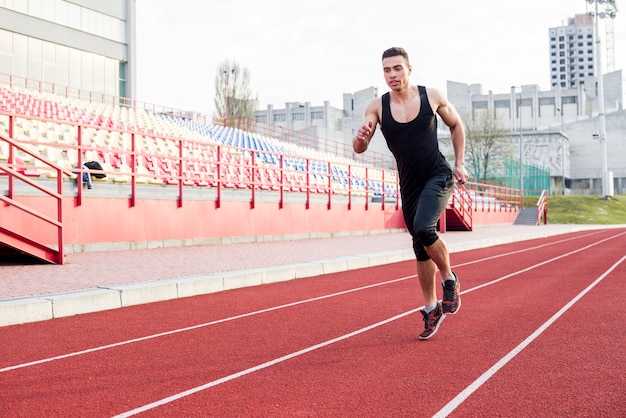 Portrait of fitness young male athlete running on race track in the stadium