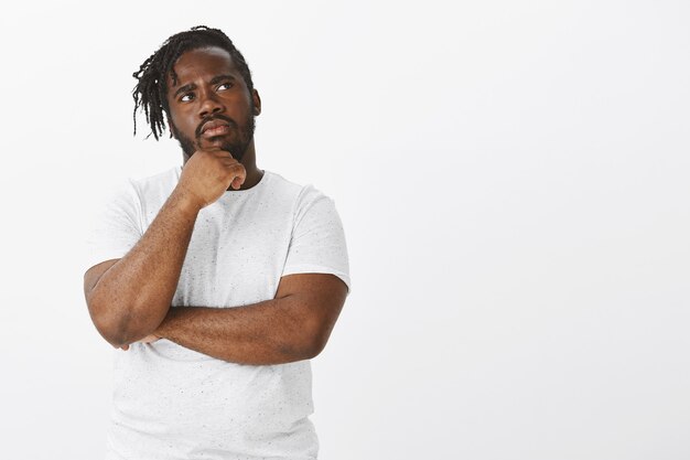 Portrait of focused guy with braids posing against the white wall