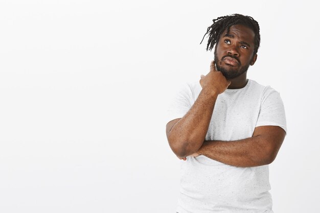 Portrait of focused guy with braids posing against the white wall