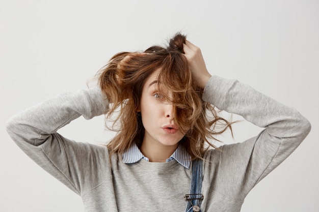 Free photo portrait of funny girl touching her beautiful auburn hair while spending day-off at home being alone. brunette woman in casual posing with pleasant facial expressions. close-up