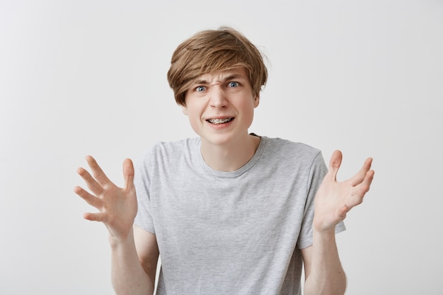 Free photo portrait of furious young caucasian male gestures in anger, being dissatisfied with results of work, screams loudly. frustarated fair-haired guy full of rage gestures against gray background.