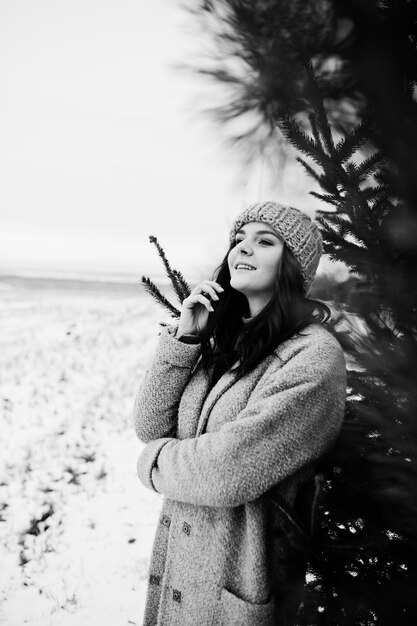 Portrait of gentle girl in gray coat and hat against new year tree outdoor