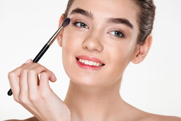 Portrait of gentle pretty woman with healthy skin applying make up painting eyes with brush