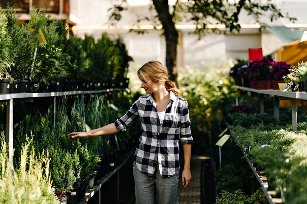 Free photo portrait of girl in black and white blouse touching bush of needles cute model with fierycolored hair poses in plant store