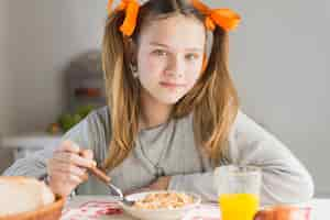 Free photo portrait of a girl eating healthy cereals with glass of juice on table