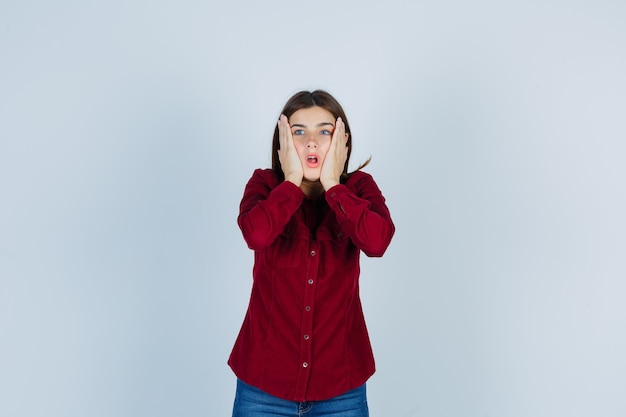 Portrait of girl holding hands on cheeks in casual shirt and looking anxious