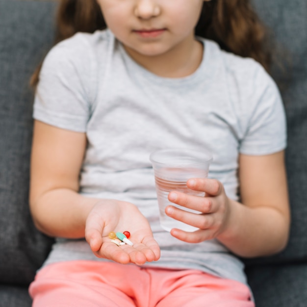 Free photo portrait of a girl holding medicine and glass of water in hand