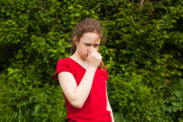 Portrait of girl holding nose in green nature looking at camera