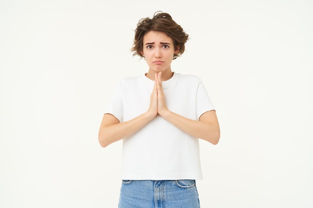 Free photo portrait of girl looking with begging face holding hands in pray pleading making wish standing over