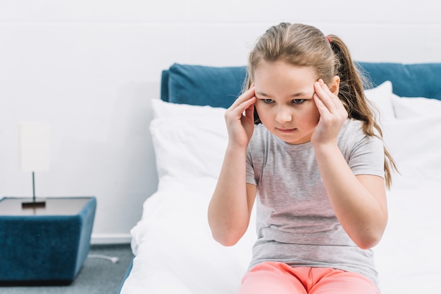 Portrait of a girl sitting on bed having headache