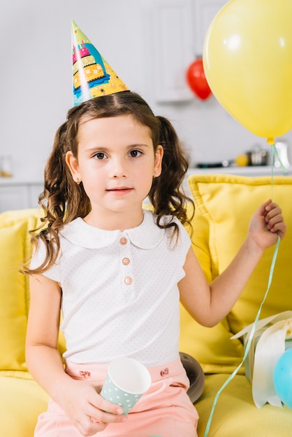 Portrait of a girl sitting on sofa holding balloon in hand