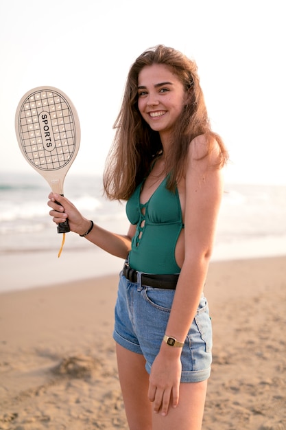 Free Photo portrait of a girl standing at beach holding tennis racket