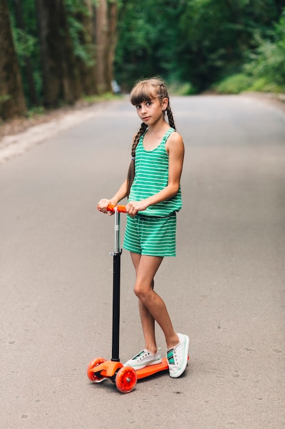 Free photo portrait of a girl standing on push scooter at street