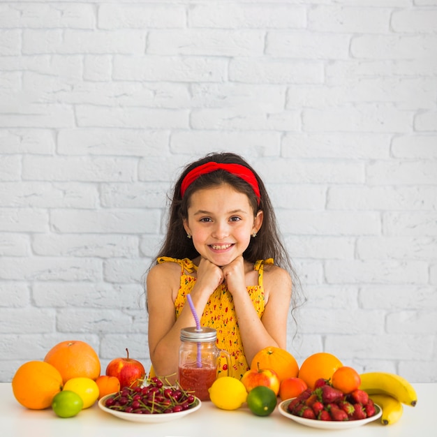 Free photo portrait of a girl standing behind table with fresh organic fruits