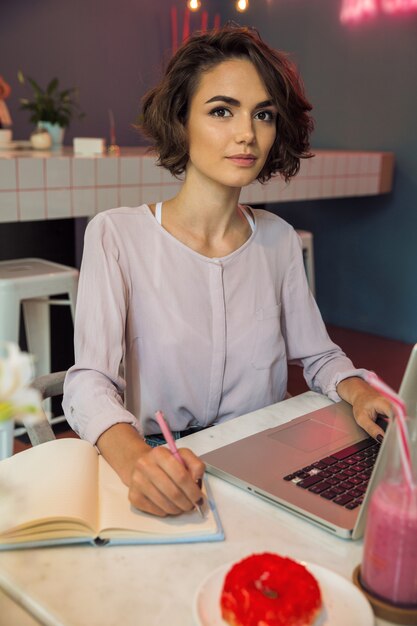 Portrait of a girl typing on laptop and writing notes