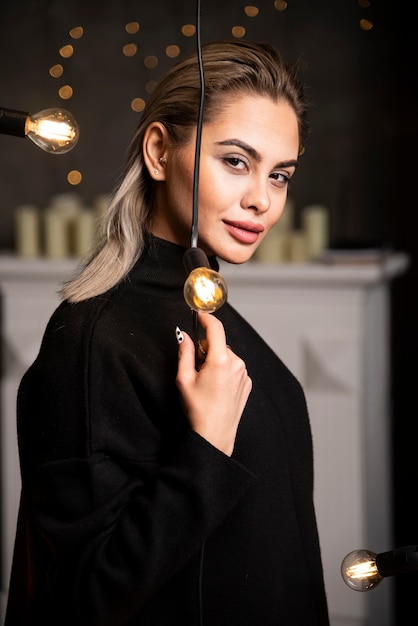 Portrait of a glad pretty woman in dark sweater standing near lamps .