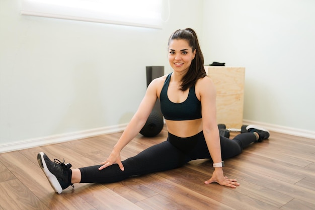 Portrait of a gorgeous brunette woman doing a leg split and smiling. Beautiful sporty woman stretching before her workout routine at home