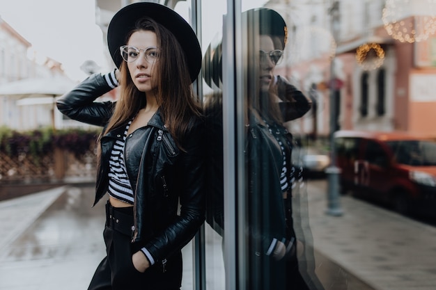 Portrait of a gorgeous woman in the city after rain near brilliant shop windows in cold weather in the day