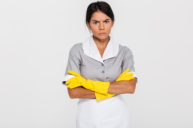 Free photo portrait of grumpy attractive maid in uniform and yellow rubber gloves standing with crossed hands